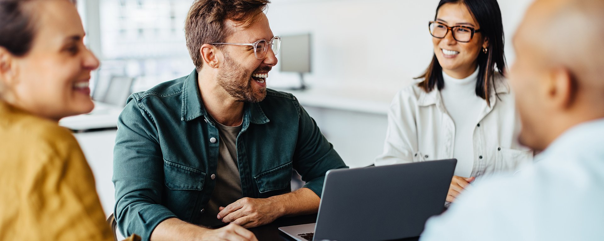 Vier Personen sitzen an einem Tisch und unterhalten sich, in der Mitte steht ein Laptop